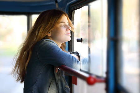 Young pretty red-haired teenage girl dreamily standing at the window facing the windの写真素材