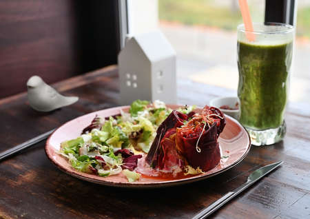 Vegetarian dish beetroot risotto with lettuce selective focus served with glass of vegetable smoothie on the wooden table by the windowの写真素材