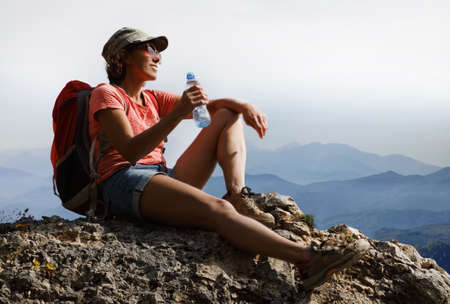 Female tourist drinking water on top of a hill in silence and loneliness admires a tranquil natural landscape in search of a soul. Theme of drinking water advertisingの写真素材