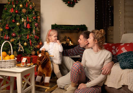 Young happy family celebrates Christmas by the fireplace and Christmas treeの写真素材