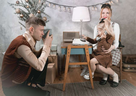 Dad shoots his family with a vintage movie camera. Retro style family in a Christmas backgroundの写真素材