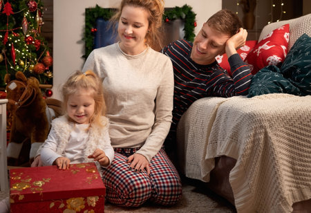 Little girl child at home by the fireplace with her young parents  and Christmas tree with giftsの写真素材