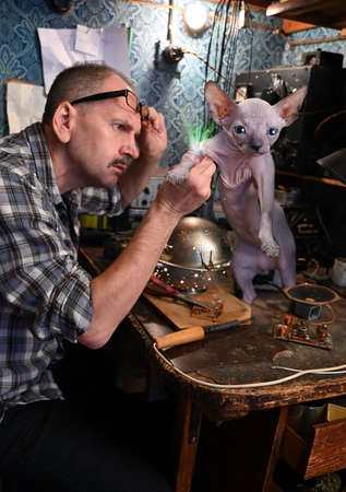 Amateur radio operator with great attention examines an unusual device on the paw of a hairless cat alien. Aliens are among usの写真素材
