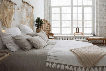 Large bed with pillows against the background of a large window flooded with daylightの写真素材