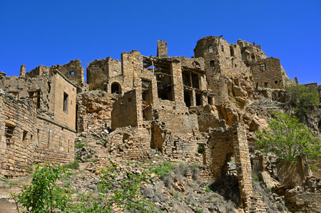 Ruins of ancient Gamsutl village with abandoned building stone walls at the top of the mountain peak against blue sky on sunny day in the Caucasus, Russiaの写真素材