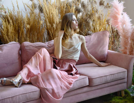 Young adult woman sitting on a sofa in a room in the middle of tall grassの写真素材