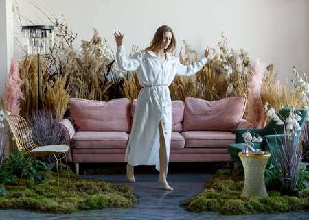 Nice young woman walks on a water filled floor in a room with sofa in the middle of tall grassの写真素材