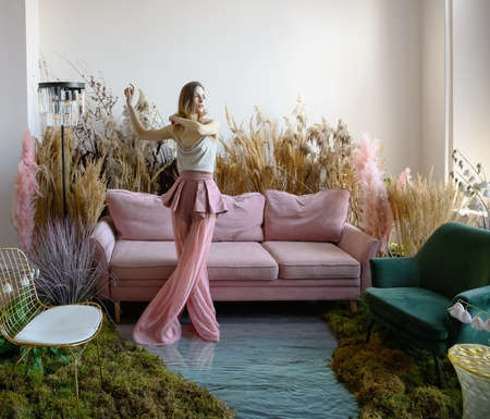 Beauty young woman dancing in a room with sofa in the middle of tall grass with the floor flooded with waterの写真素材