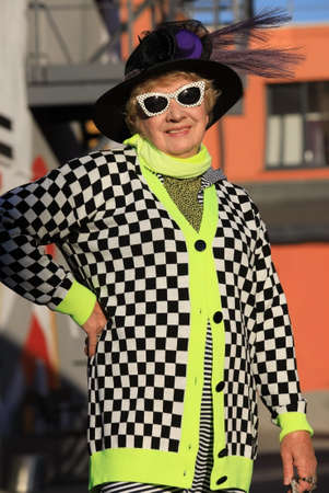 Stylishly dressed elderly retired woman in sunglasses walks on a city street on a sunny autumn dayの写真素材