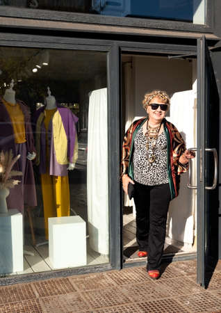 Stylishly dressed granny comes out of a fashion boutique, autumn sunny dayの写真素材