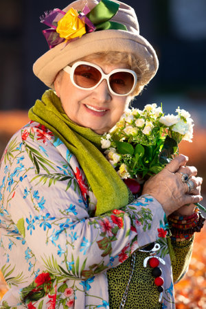 Portrait of a smiling eighty year old senior woman with a bouquet of flowers outdoors on an autumn sunny dayの写真素材