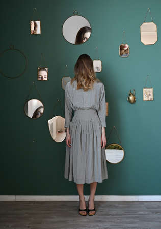 Conceptual portrait of a young woman in a dress with a reflection of her face in various mirrorsの写真素材