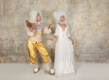 Caucasian couple in Baroque style clothes and white wigs  reading a book indoorsの写真素材
