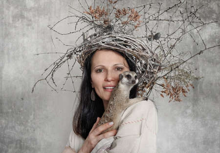Portrait of a young woman with a wreath of vines and a meerkat on her shoulderの写真素材