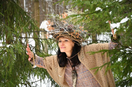 Portrait of a young adult woman with a wreath of twigs on her head in a wild winter forestの写真素材