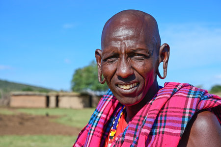 MAASAI MARA NATIONAL RESERVE, KENYA, AFRICA - NOVEMBER 11, 2022: Maasai village with maasai tribe. Portrait of a maasai man against the blue sky in maasai village in Kenya, Africaのeditorial素材