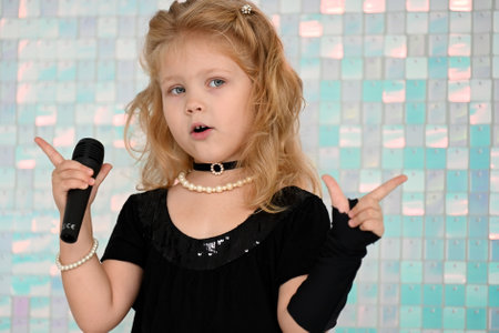 Portrait of a cute little girl in a black dress singing karaoke in the studioの写真素材