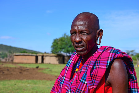 MAASAI MARA NATIONAL RESERVE, KENYA, AFRICA - NOVEMBER 11, 2022: Portrait of a maasai man in traditional colorful clothing against the blue sky in maasai village in Kenya, Africaのeditorial素材