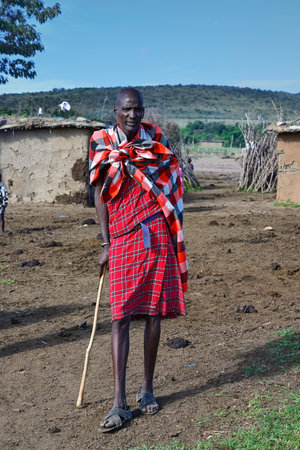 MAASAI MARA NATIONAL RESERVE, KENYA, AFRICA - NOVEMBER 11, 2022: Maasai village with maasai tribe. Maasai man in traditional colorful clothing standing in the middle of a Maasai village in Kenya, Africaのeditorial素材