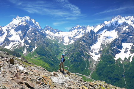 Tourist adult woman stands on the top of a mountain and admires the beautiful views of the mountains on a sunny dayの写真素材