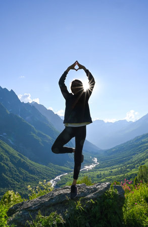 Young adult woman poses against the background of mountains backlit by the midday sun