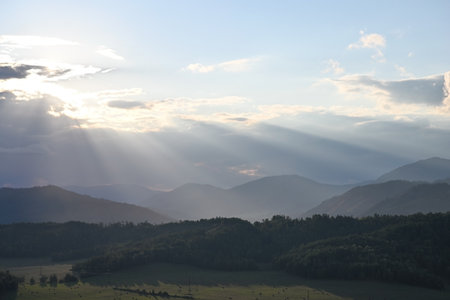 The rays of the sun at sunset break through the cumulus clouds over the valley and mountains. Natural landscape on a summer dayの写真素材