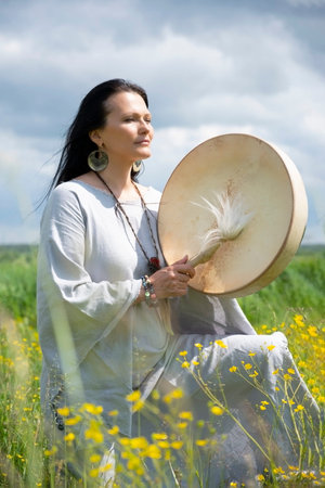 Portrait of a middle-aged shaman woman drumming among yellow flowers