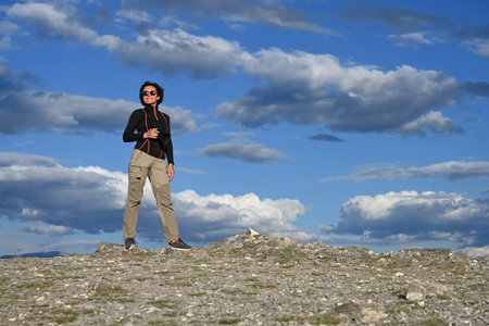 Middle-aged female tourist with a camera hiking in the mountains against the background of a picturesque blue skyの写真素材