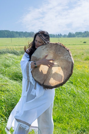 Female shaman in the white dress drumming in the natural environmentの写真素材