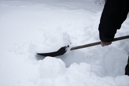 Manual cleaning of snow in winter. Plastic black shovel with wooden handle.の写真素材