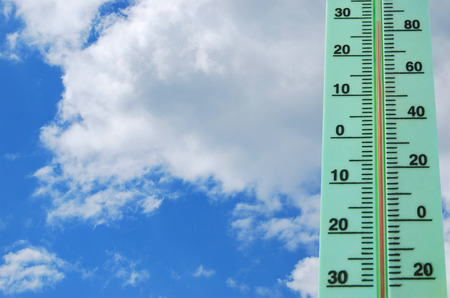 Street thermometer with high temperature against a blue sky with white cloudsの写真素材
