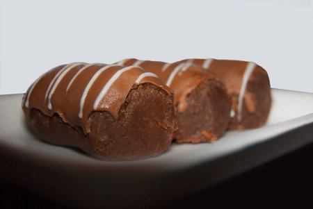 Three cakes Kartoshka lie in a row on a white rectangular plate. On a light background.