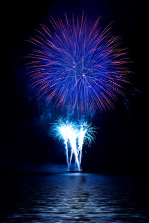Colorful fireworks in the night sky and reflecting on the waterの写真素材