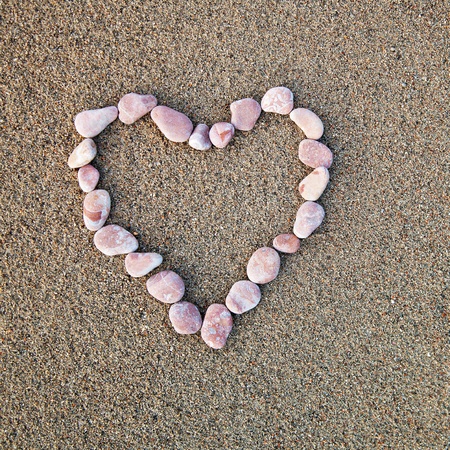 Heart of pebbles inlaid on a background of sand. Can be used as backgroundの写真素材