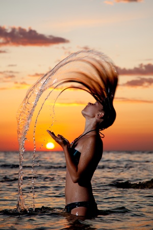 A young girl in the sea with a beautiful splashes of water from the hair at sunsetの写真素材