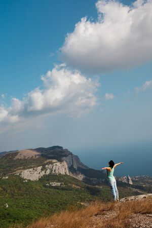 Girl with hands up on the background of mountains and blue sky with cloudsの写真素材