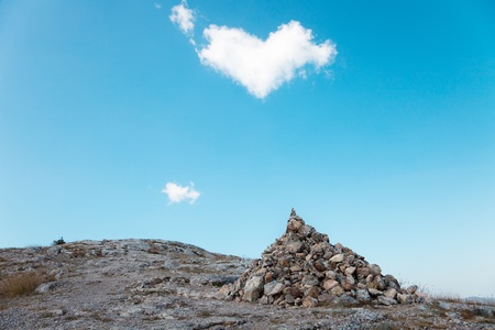 A pile of stones on the ground under a blue sky and a passing cloud in the shape of heartの写真素材
