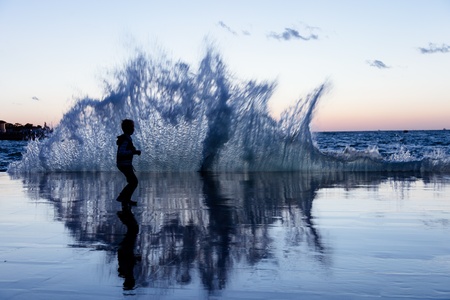 The silhouette a child on the seafront running away from the wavesの写真素材