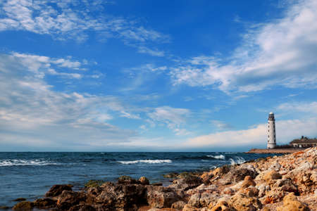 Seascape  Lighthouse by the sea on a background of blue sky with cloudsの写真素材