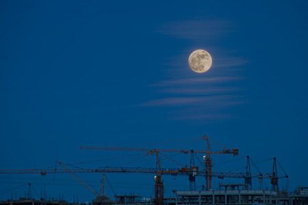 Construction cranes at dusk in the light of the full moonの写真素材