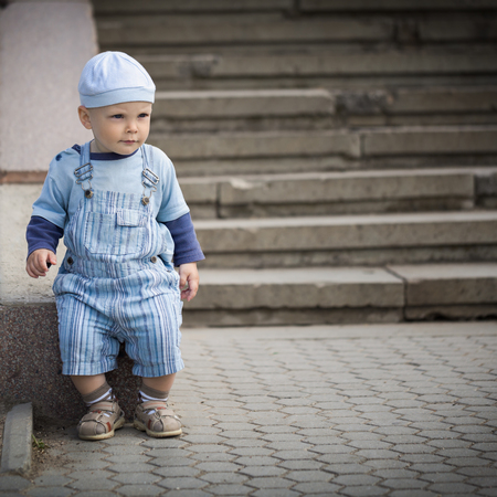 Little boy in hat standing by the stairsの写真素材