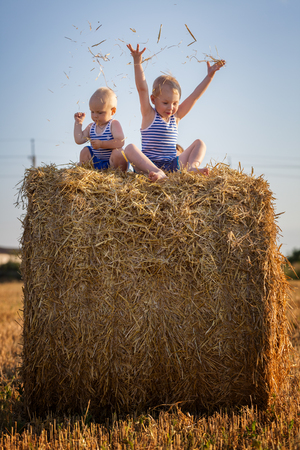 Small children play sitting on a haystackの写真素材