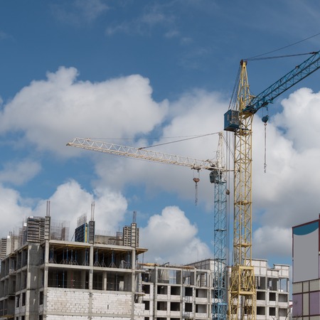 Construction cranes tower above the construction site, against a blue sky with cloudsの写真素材
