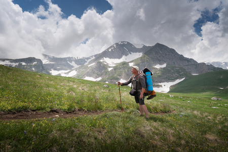 Tourist with a large backpack on the pathway in the background of high snow-capped mountainsの写真素材