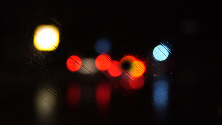 Night city in the lights of street lamps. Defocused view through the wet glass of the carの写真素材