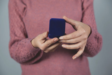 woman hand holding blue ring  box on gray background