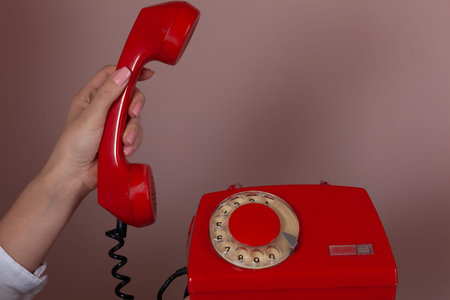 woman hand holding red vintage phone on pink background