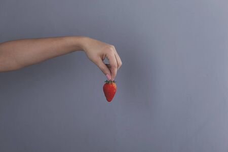 woman hand holding strawberry on grey backgroundの写真素材