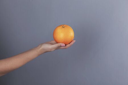 woman hand holding orange on grey backgroundの写真素材