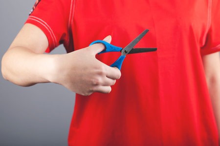 woman hand holding blue scissors on gray background